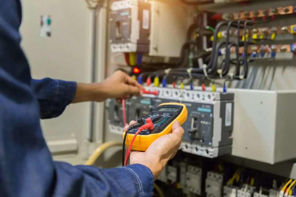 Technician measuring voltage with a multimeter in an electric panel.