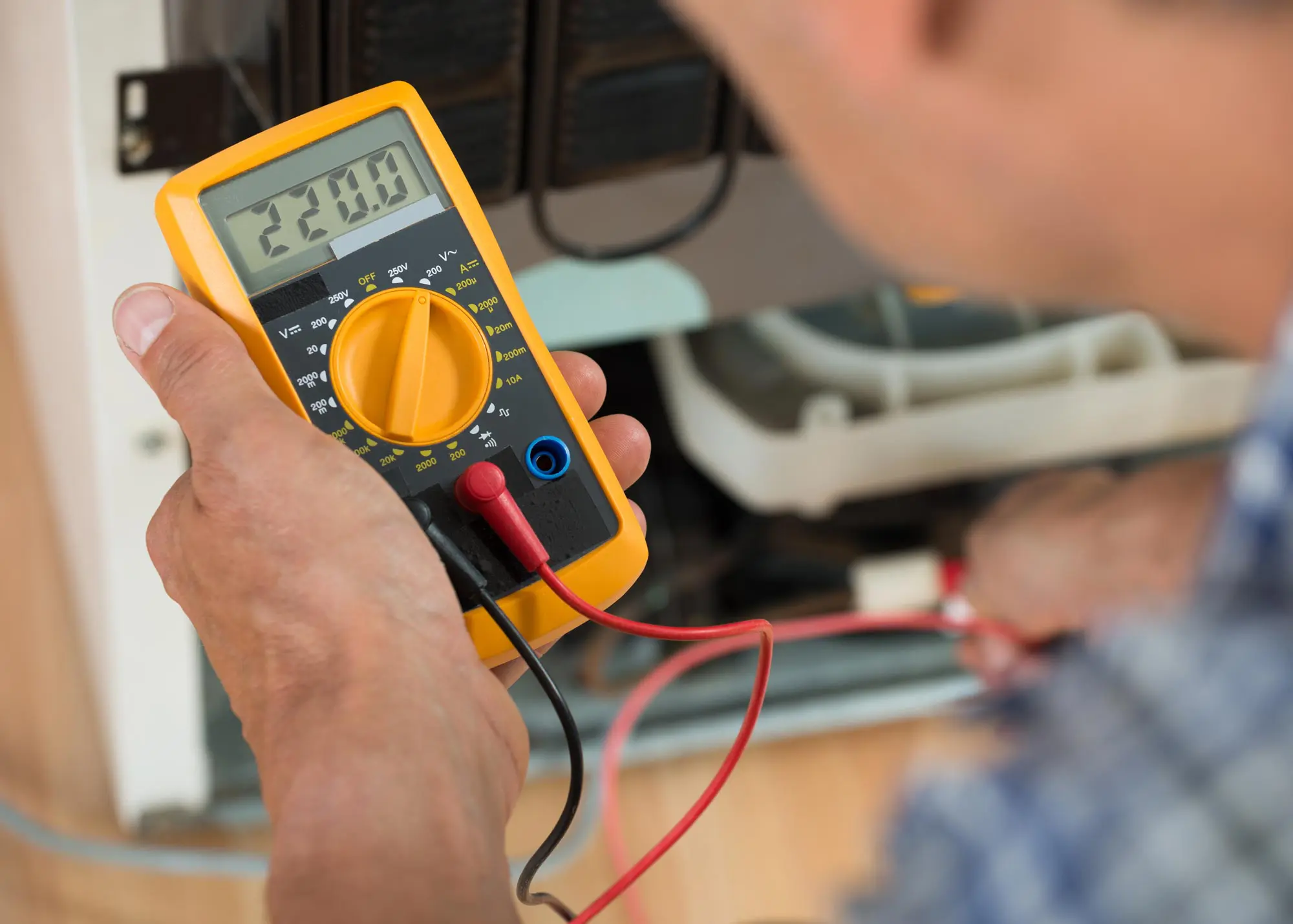 A person checking voltage with a multimeter reading 220.0.