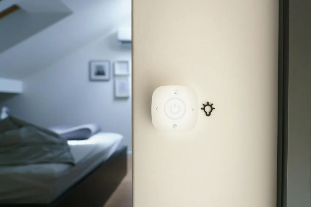 Smart light switch mounted on a wall near a blurred bedroom.